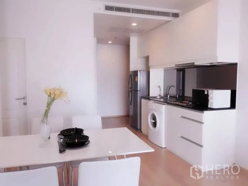 Condominium for rent in Bangkok - Compact kitchen with white cabinetry, hob, fridge, microwave and in‑unit washing machine.