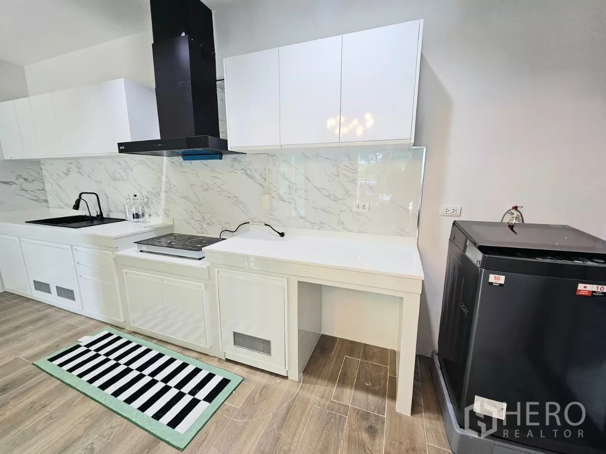 Townhouse for rent in Saphan Sung, Bangkok - Kitchen counter with cooktop, range hood, ample cabinetry and large appliance.