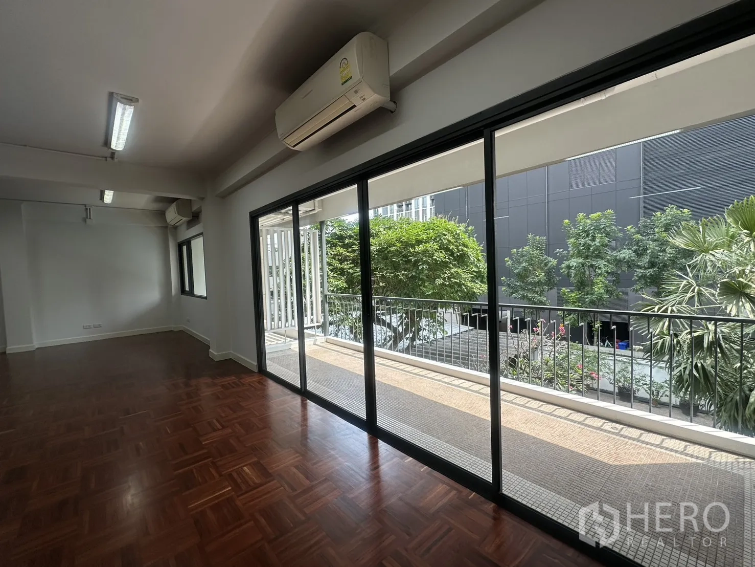 Office Space for rent in Watthana, Bangkok - Sliding glass doors leading to a long balcony overlooking trees and a modern building.