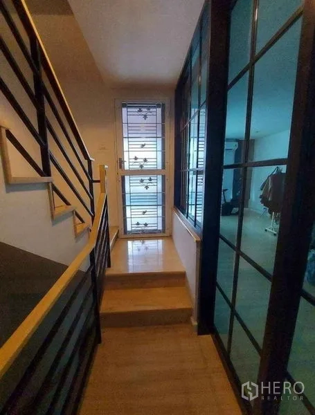 Townhouse for rent in Bang Phli, Samut Prakan - Interior corridor with wooden stairs, metal handrail and glass partition leading to living area.