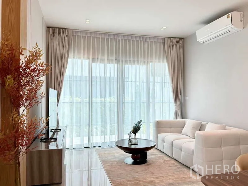 Detached House for rent or sale in Bang Phli, Samut Prakan - Living room with white sofa, sliding glass doors, sheer drapes and air conditioning.