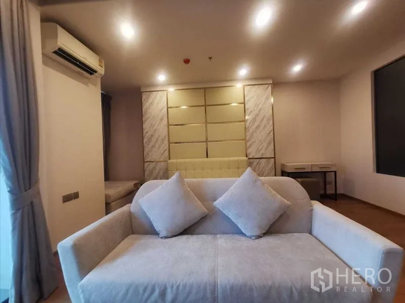 Condominium for rent in Ratchathewi, Bangkok - Cozy studio-style seating area with soft-lit sofa beside the sleeping zone.
