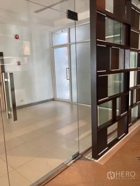 办公空间 出租在Khlong Toei, Bangkok - 玻璃墙办公室入口，磨砂门、瓷砖地面与现代格栅式隔断。