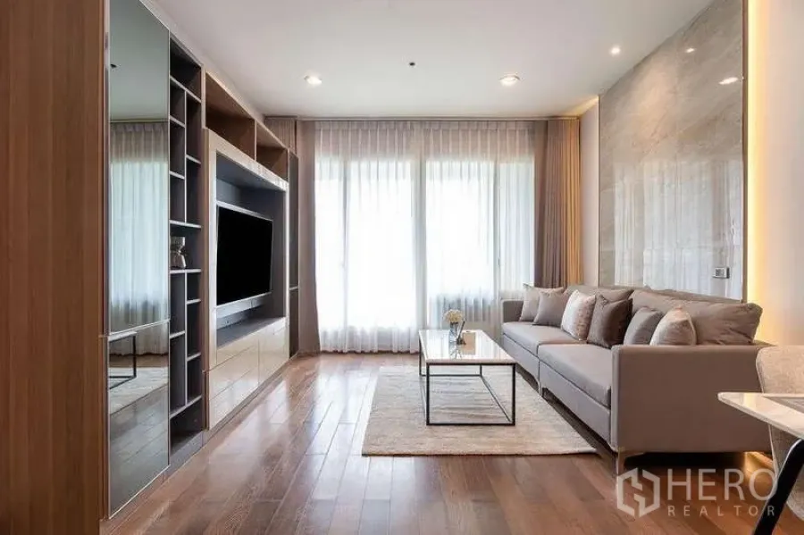 Condominium for rent in Pathum Wan, Bangkok - Living area facing the balcony, showcasing sofa, media wall, and bright natural light.