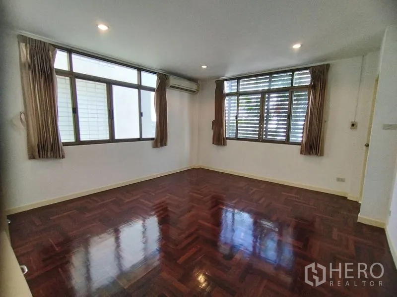 Detached House for rent in Watthana, Bangkok - Corner bedroom with large windows, air-conditioning, and polished wood floor.