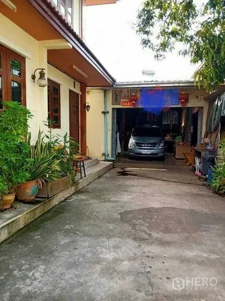 บ้าน ขายในBang Na, Bangkok - ทางรถเข้าพร้อมโรงจอดรถ มีต้นไม้กระถางและพื้นที่จอดข้างตัวบ้าน