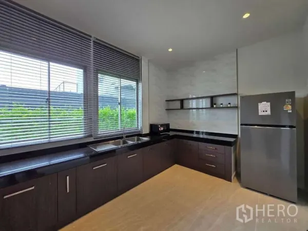 Detached House for rent or sale in Lat Krabang, Bangkok - Bright L-shaped kitchen with large windows, dark cabinets, and stone countertops.