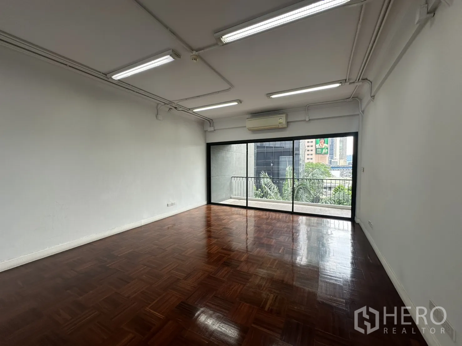 Office Space for rent in Watthana, Bangkok - Private office room with glossy wooden flooring and large sliding glass doors to the balcony.