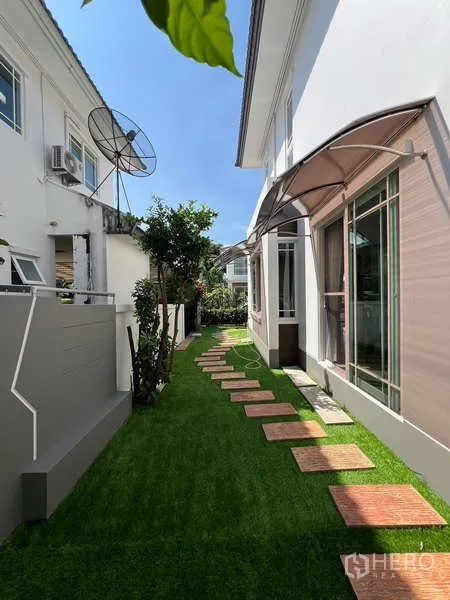 独立式住宅 出租在Bang Kapi, Bangkok - 现代白色立面旁的侧院草坪与踏步石步道。