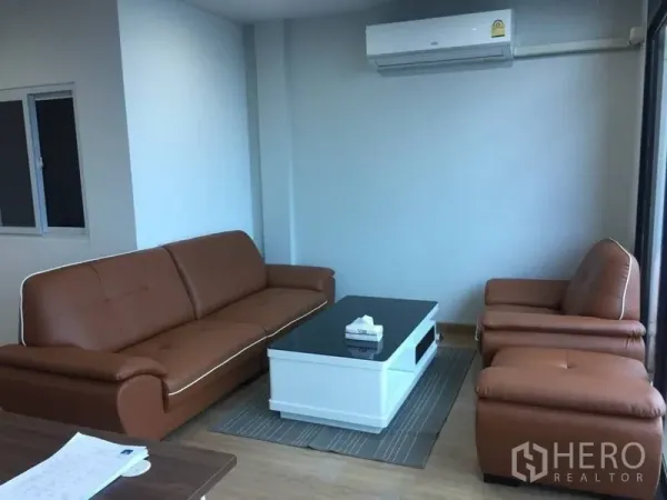 带办公室的家 出租或出售在Prawet, Bangkok - 带棕色皮沙发与白色茶几的会客区，墙挂式空调，明亮整洁。