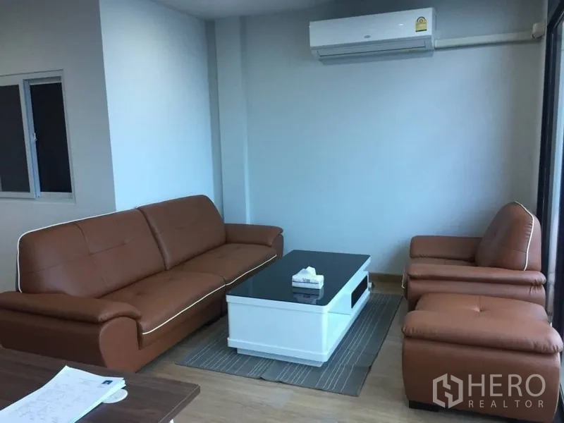 带办公室的家 出租或出售在Prawet, Bangkok - 带棕色皮沙发与白色茶几的会客区，墙挂式空调，明亮整洁。