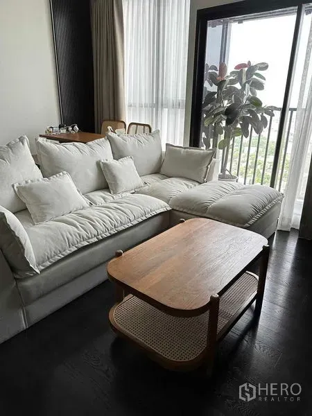 Condominium for rent in Khlong Toei, Bangkok - Corner lounge with plush sectional sofa, wooden coffee table and floor-to-ceiling windows to balcony.