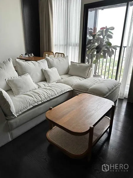 Condominium for rent in Khlong Toei, Bangkok - Corner lounge with plush sectional sofa, wooden coffee table and floor-to-ceiling windows to balcony.