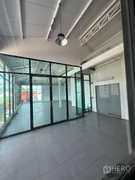 零售空间 出租在Bang Na, Bangkok - 带玻璃隔断与双扇滑门的入口，工业风吊灯与瓷砖地面，现代感十足。
