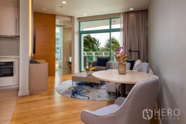 Condominium for rent in Bang Kho Laem, Bangkok - Dining corner and living space with round table and armchairs, wood flooring, and balcony-height glazing.