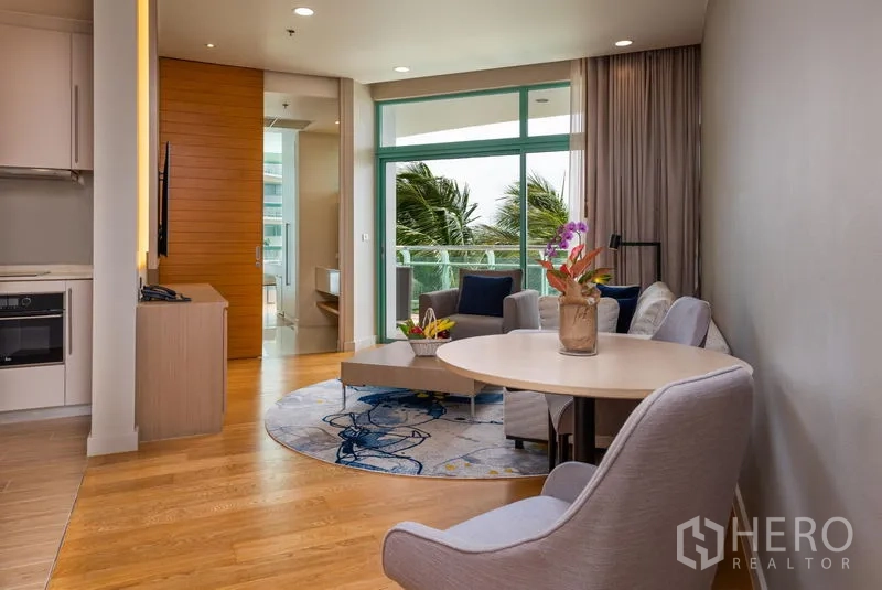 Condominium for rent in Bang Kho Laem, Bangkok - Dining corner and living space with round table and armchairs, wood flooring, and balcony-height glazing.