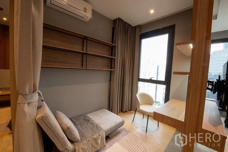 Condominium for rent in Din Daeng, Bangkok - Flexible den or study with wall shelving, daybed and a window facing the urban skyline.
