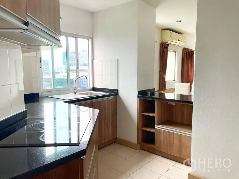 Condominium for rent in Khlong Toei, Bangkok - Kitchen close-up showing black countertops, storage and window with cityscape view.