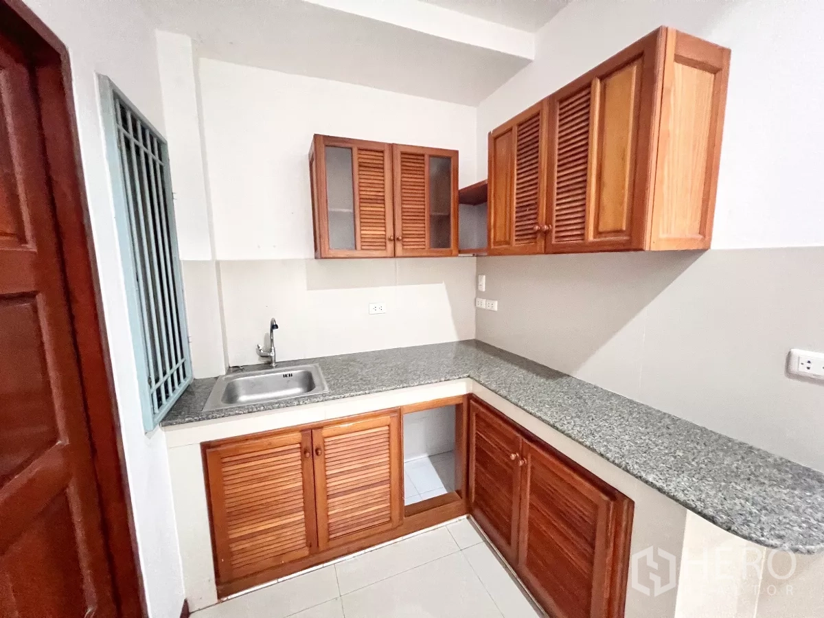 Townhouse for rent or sale in Phra Khanong, Bangkok - Main kitchen with granite countertop, sink and wooden louver cabinets.