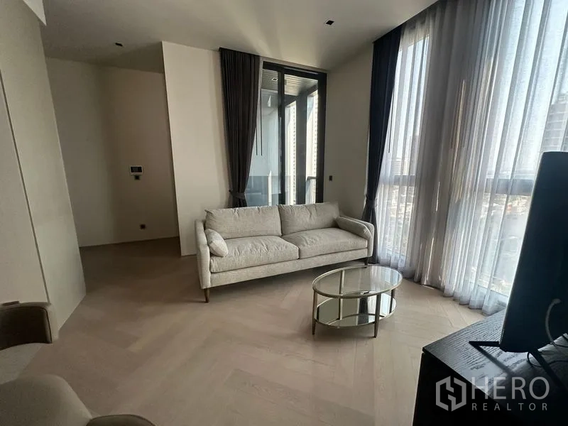 Condominium for rent - Corner lounge with sofa and glass coffee table beside full-height windows and a glass door.