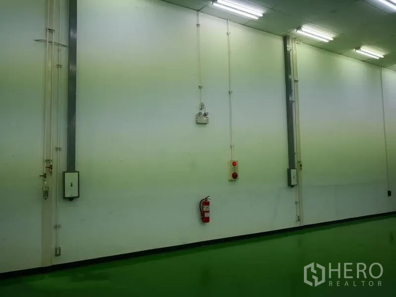 Warehouse for rent in Bang Phli, Samut Prakan - Close-up of warehouse wall showing electrical conduit, emergency buttons and a fire extinguisher.