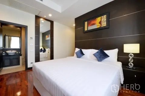 อพาร์ทเมนท์ for rent in Watthana, Bangkok - ห้องนอนใหญ่ผนังแต่งโทนเข้ม โคมไฟข้างเตียง และทางเข้าห้องน้ำในตัว