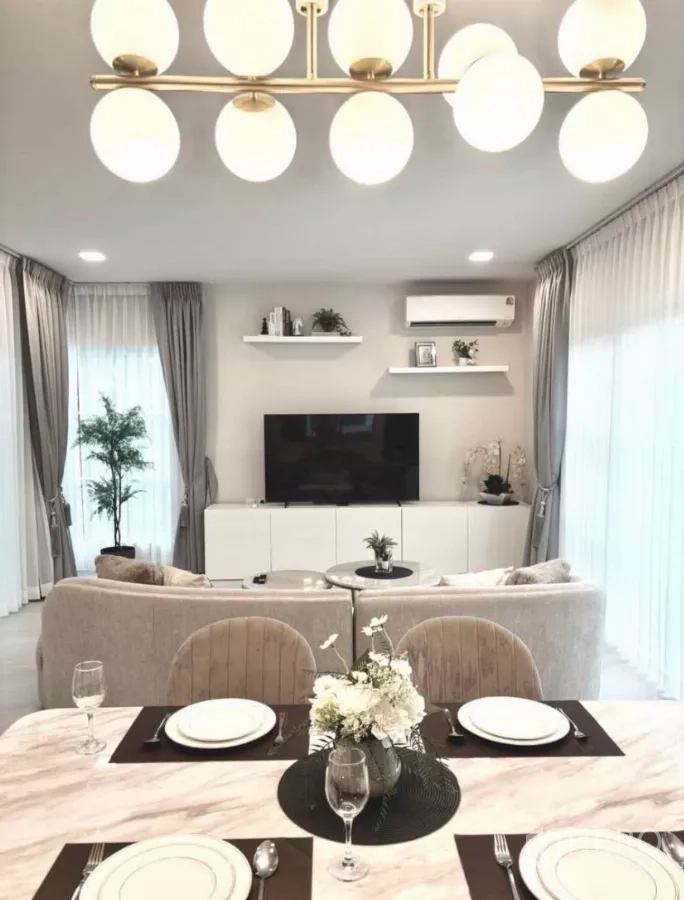 独立式住宅 出租在Bang Phli, Samut Prakan - 餐桌对着电视墙，吊灯与薄纱窗帘。