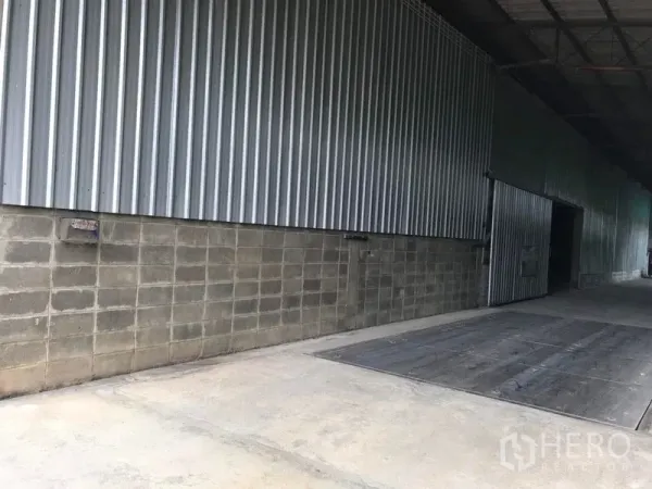 Warehouse for rent in Mueang Nakhon Pathom, Nakhon Pathom - Covered loading dock along a corrugated steel wall with a wide sliding door.