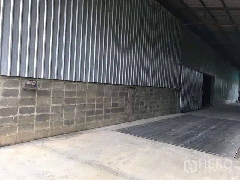 Warehouse for rent in Mueang Nakhon Pathom, Nakhon Pathom - Covered loading dock along a corrugated steel wall with a wide sliding door.