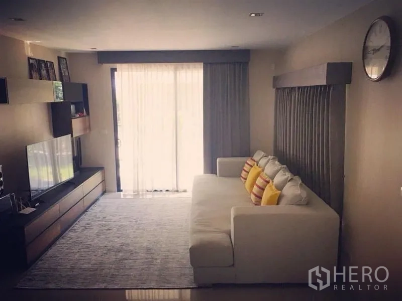 Detached House for sale - Bright living room with white sofa, TV wall, and sliding glass doors with sheer curtains.