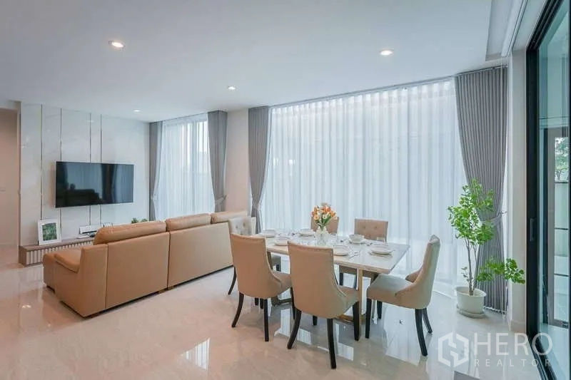 Detached House for rent in Bang Phli, Samut Prakan - Open-plan living and dining area with wall-mounted TV and floor-to-ceiling windows.