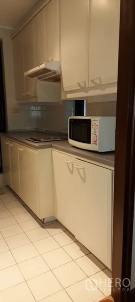 Condominium for rent in Sathon, Bangkok - Galley kitchen with white cabinets, cooktop, range hood and microwave.