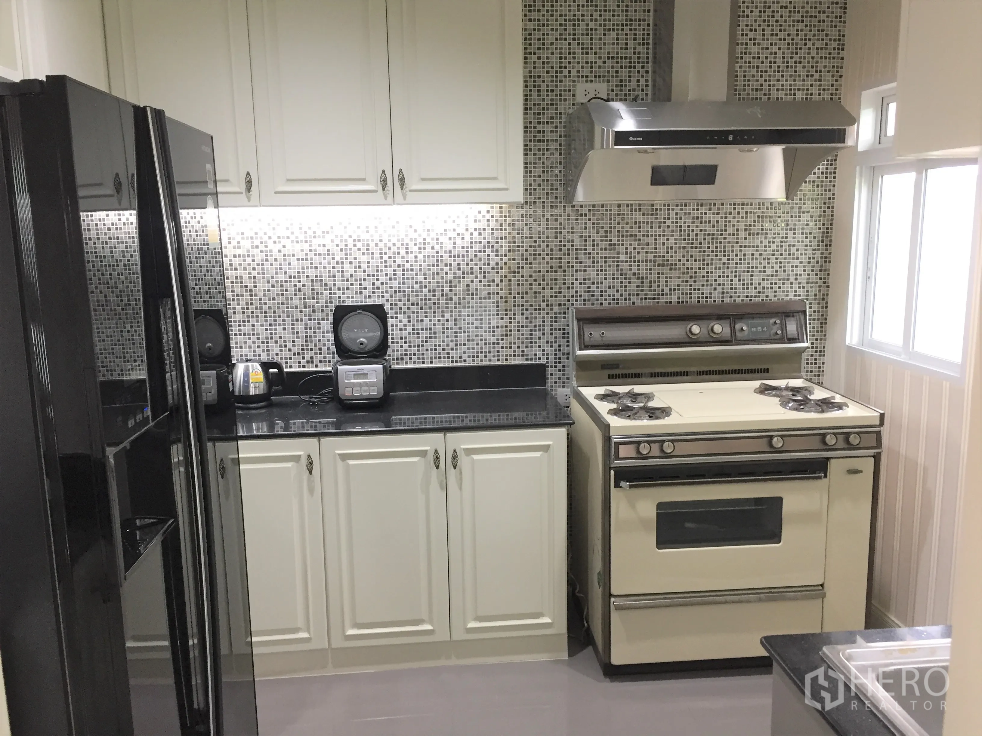 Detached House for rent in Saphan Sung, Bangkok - Fitted kitchen with mosaic backsplash, gas stove, range hood and a large black refrigerator.