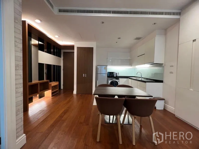 Condominium for rent in Khlong Toei, Bangkok - Open living–dining space with wooden flooring and fitted cabinetry leading to the kitchen.