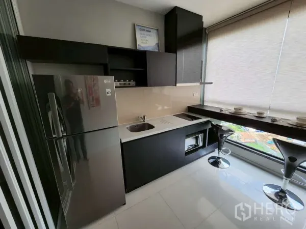 Condominium for sale - Modern kitchenette with black cabinetry, fridge, cooktop, microwave and a window breakfast bar with stools.