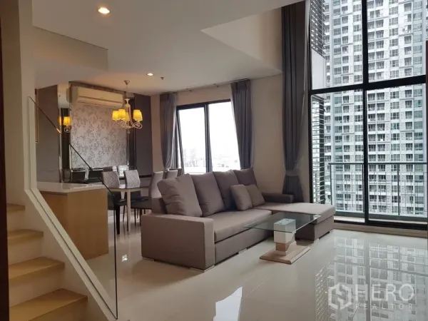 Condominium for rent in Ratchathewi, Bangkok - Bright duplex living room with L-shaped sofa, dining area, and floor-to-ceiling windows overlooking the Bangkok skyline.