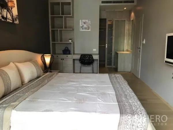 Condominium for rent in Bangkok - Spacious bedroom with built-in desk, shelving, and entrance to an ensuite bathroom.
