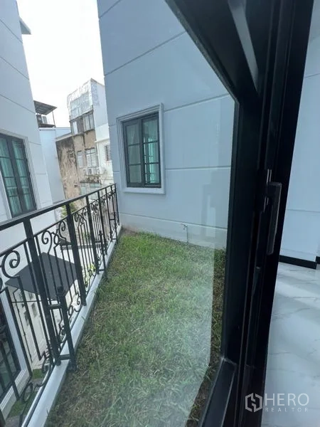 带办公室的家 出租或出售在Watthana, Bangkok - 建筑侧边的小草坪阳台花园，配黑色栏杆。