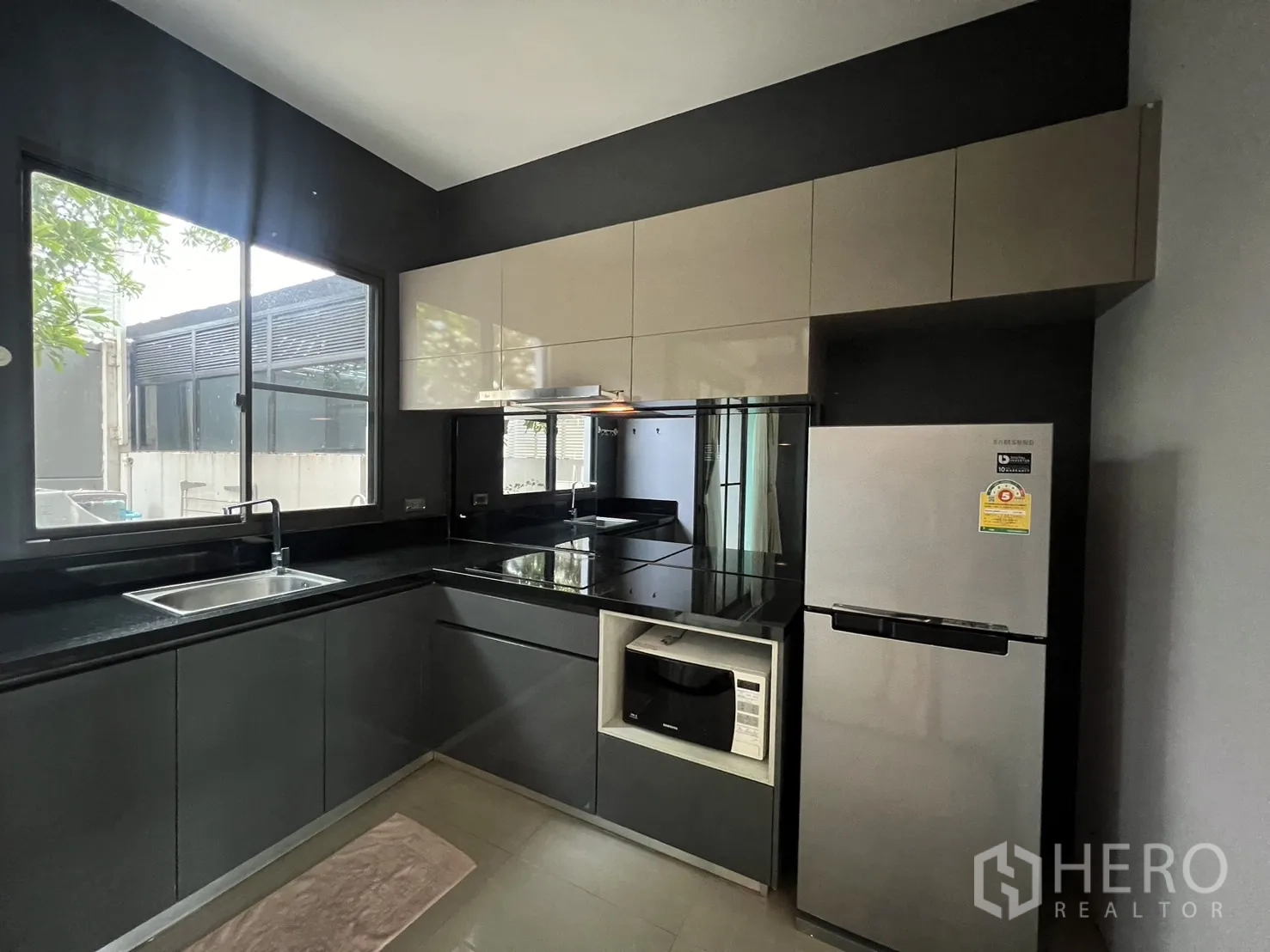 Townhouse for rent in Lat Phrao, Bangkok - Contemporary L-shaped kitchen with window, built-in cabinets, electric hob, oven and stainless fridge.