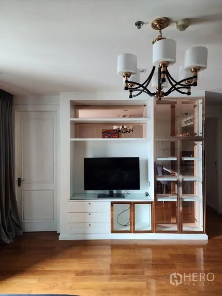 Condominium for rent in Bang Rak, Bangkok - Living room with built‑in TV wall, display shelving, chandelier and polished wood flooring.