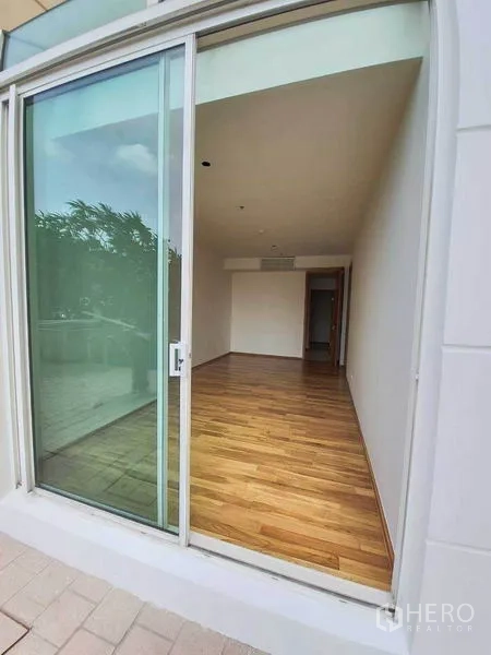 Condominium for rent or sale in Sathon, Bangkok - Ground-floor condo room with floor-to-ceiling sliding glass door, hardwood floors, and terrace greenery.