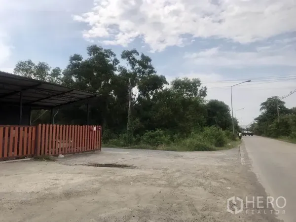 Warehouse for rent in Pathum Thani - Side angle of the warehouse beside a quiet two-lane road with streetlights, trees, and ample roadside parking space.
