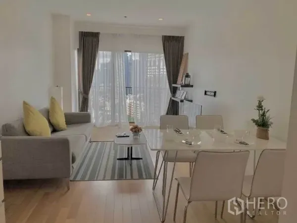 Condominium for rent in Bangkok - Living room facing large windows with sheer curtains, gray sofa and six-seat dining table.