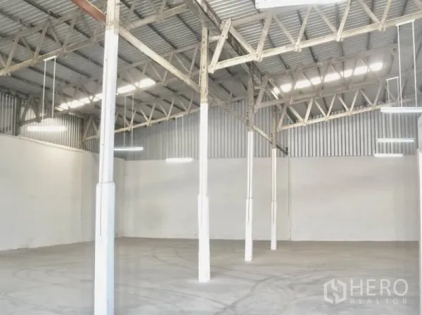 Factory for rent in Bang Pakong, Chachoengsao - High-ceiling warehouse bay showing exposed beams, hanging lights and smooth concrete floor.