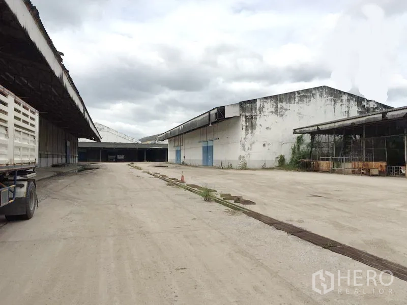货栈 出租在Pathum Thani - 室外装卸及通行区域，多栋仓库外立面与蓝色大门，适合重型卡车。