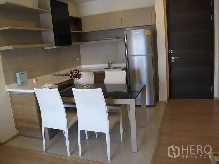 Condominium for rent or sale in Khlong Toei, Bangkok - Compact L-shaped kitchen with dining table and stainless-steel refrigerator near the entry door.