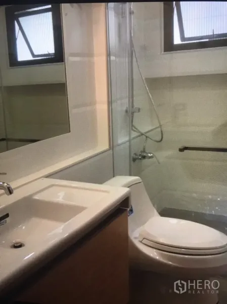 Condominium for rent in Bang Rak, Bangkok - Bathroom with large mirror, glass shower enclosure and vanity under a window.