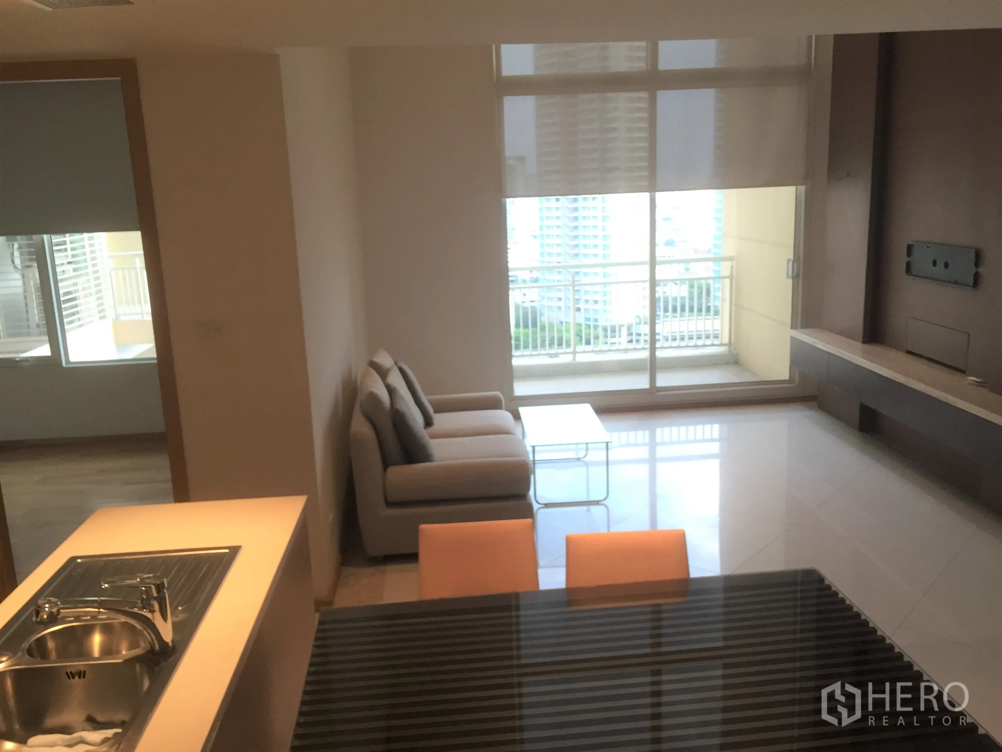 คอนโด ให้เช่าในSathon, Bangkok - ห้องนั่งเล่นสว่าง โซฟา ผนังทีวีบิลท์อิน และประตูกระจกสไลด์ออกสู่ระเบียงชมวิวเมือง