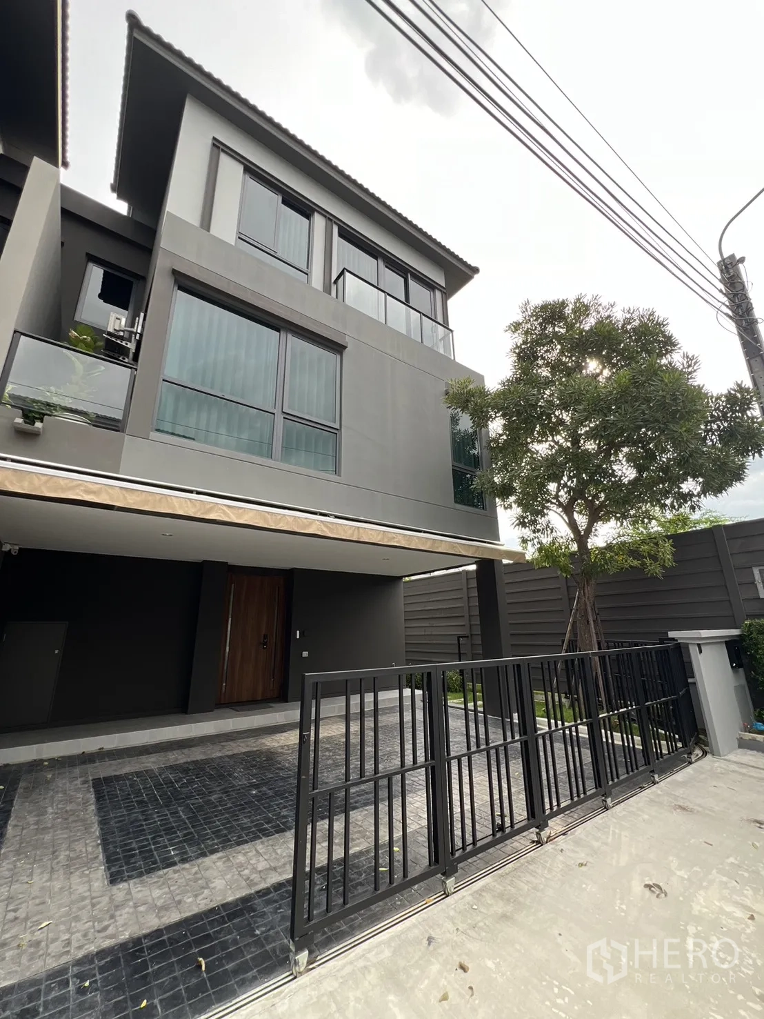 独立式住宅 出租在Prawet, Bangkok - 灰色立面与车道斜角外观，滑动栅栏门。