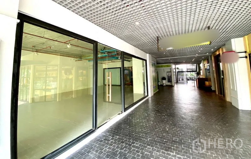 零售空间 出租在Khlong Toei, Bangkok - 商铺临室内走廊，整面黑框玻璃门面与网格天花。